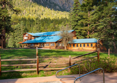 Outdoor swimming pool in foreground with wood cabin in background with mountain and pine trees
