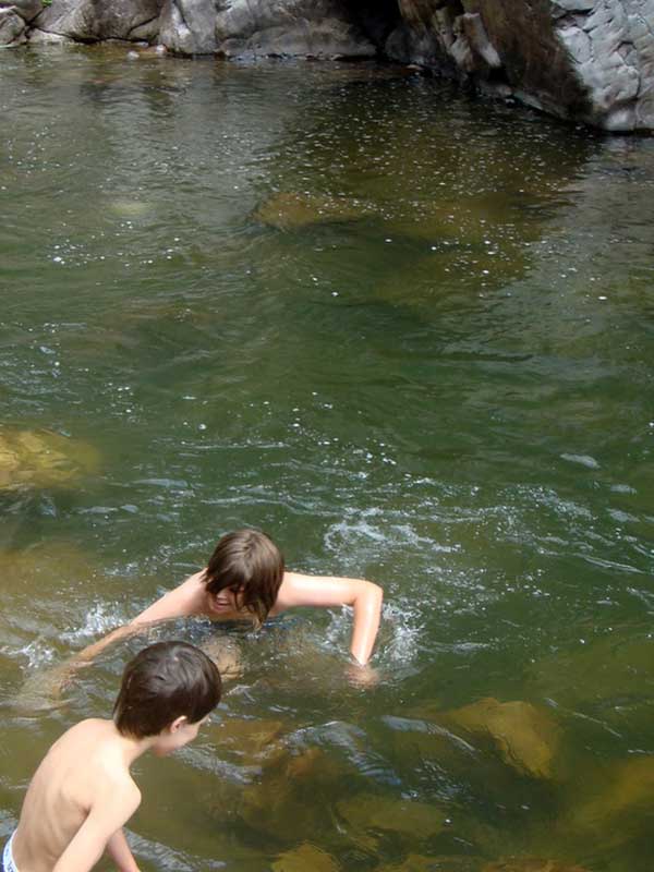 Two boys swimming in river with rocks