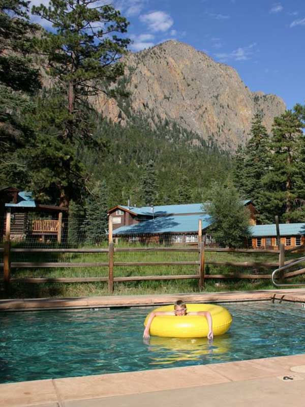 Child in yellow inner tube in swimming pool with cabins in background