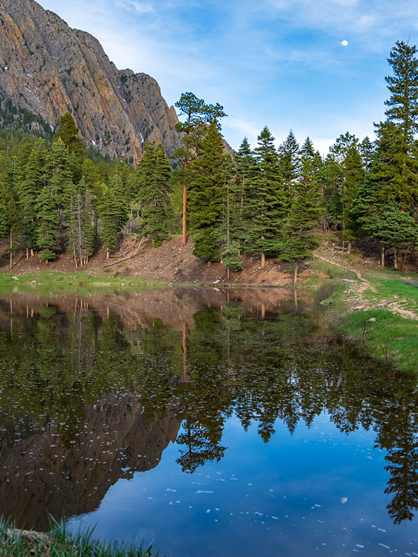 Pond with water reflecting cliffs and pine trees and blue sky