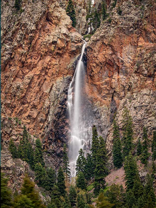 Giant thin white waterfall against red rocks with trees