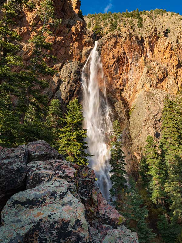 giant waterfall that is thin and white against orange rocks with trees at base