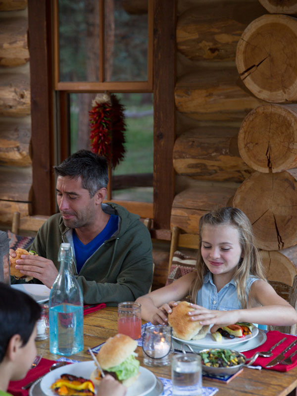 Man and girl eating hamburgers with log cabin in background