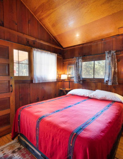 Red bedspread on bed with 2 nightstands, windows, wooden walls, ceiling and floors