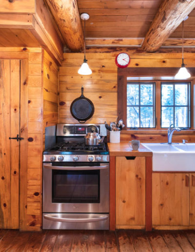 Knotty pine wooden kitchen with stainless steel oven and stove and farmhouse sink with window
