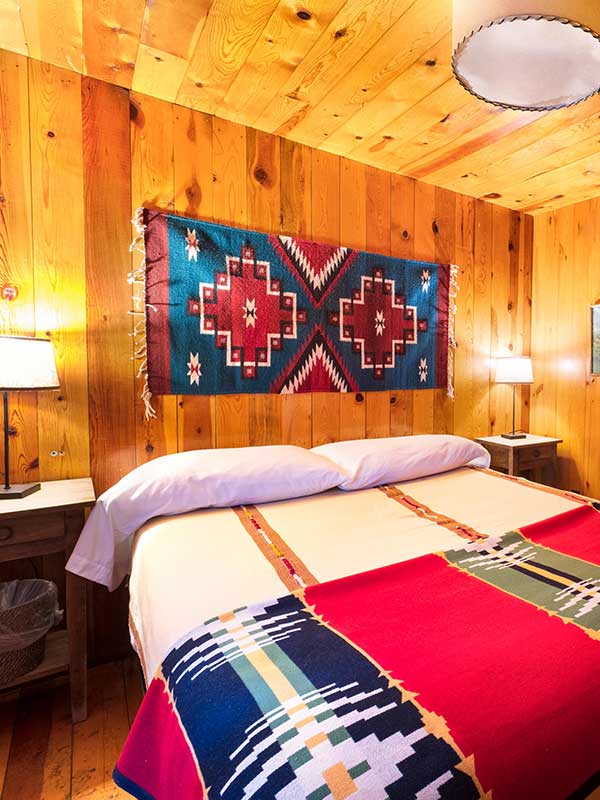 King Bed in wooden bedroom with nightstands and nightlights and red and blue native rug on wall