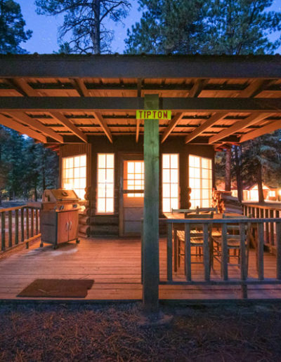 Wood cabin at dusk with lights shining through windows and tall pine trees