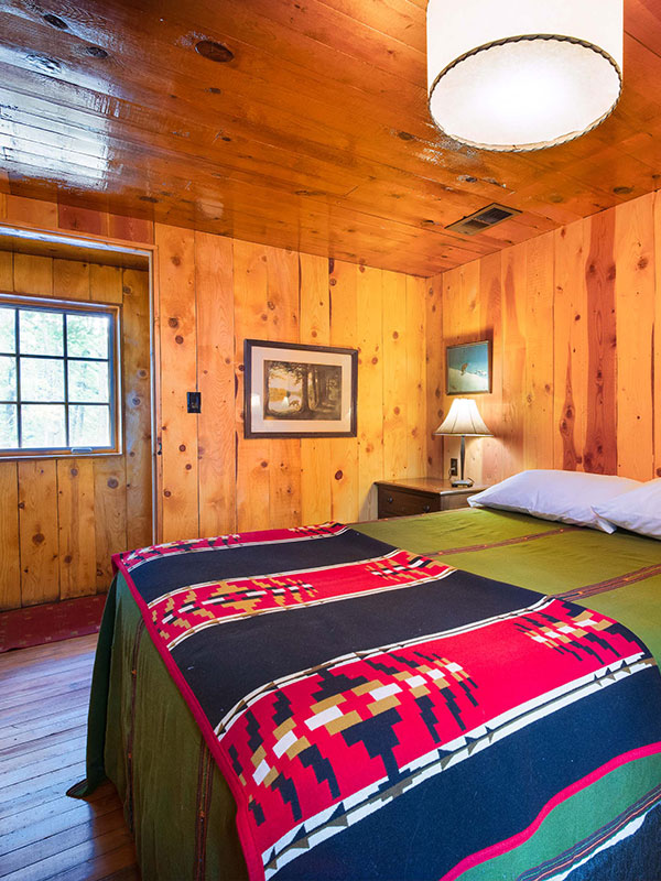 Bed with red and blue throw and green bedspread, wood walls, ceiling and floors