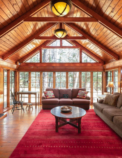 Living room with red rug, 2 couches, A-frame Wood Ceiling, Wood burning stove, coffee table, views of forest