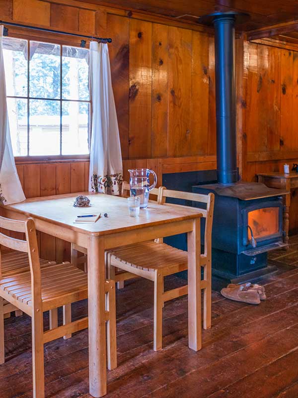 Wooden table and chairs with wood burning stove in wood paneled cabin interior