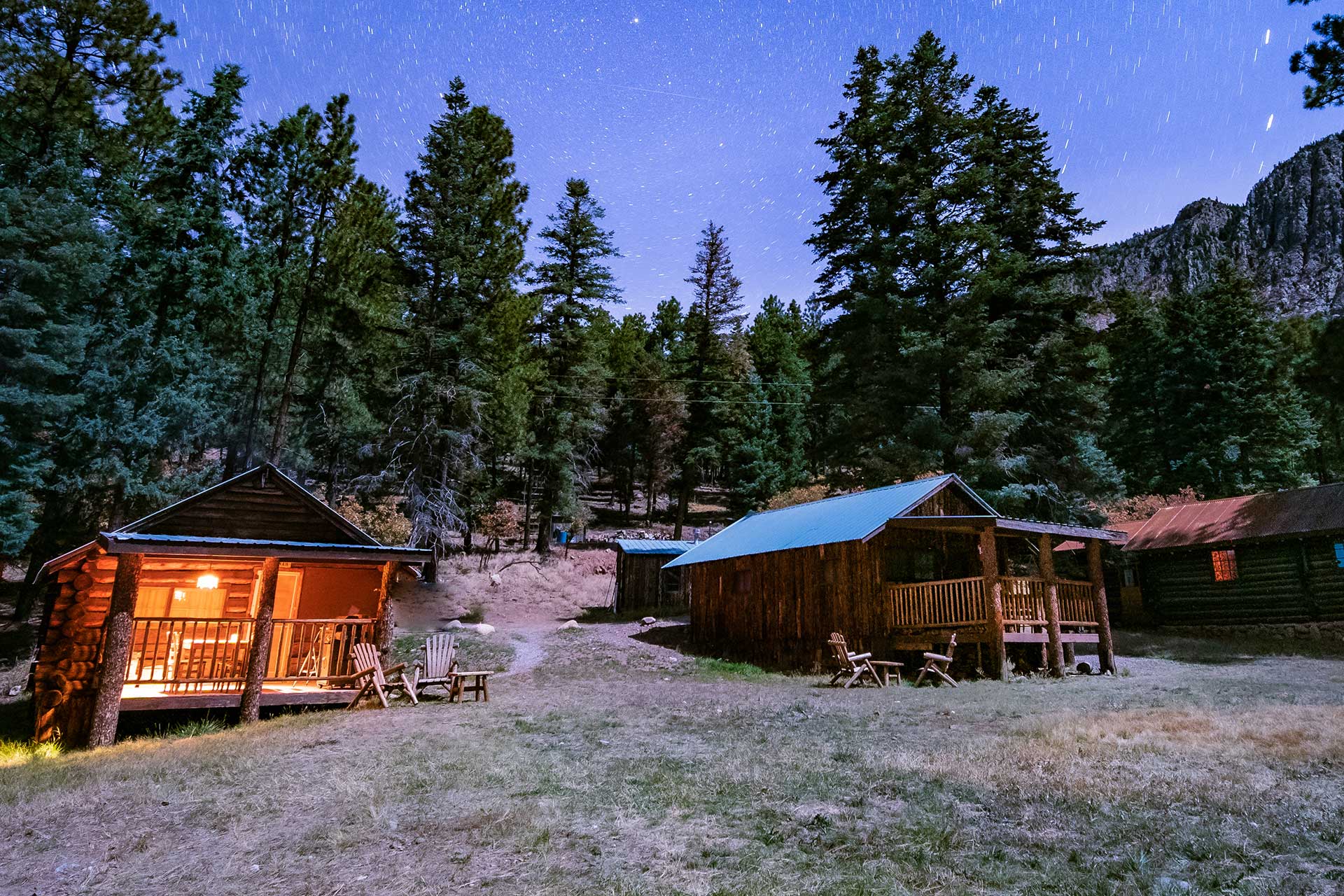 3 log cabins at night with pine trees and stars in blue sky