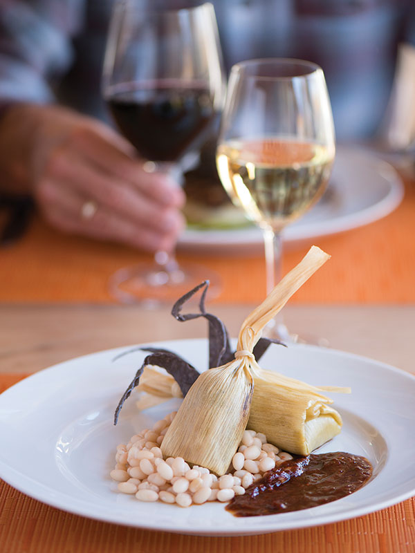 Tamales with beans and red chile on a plate with wine in the background