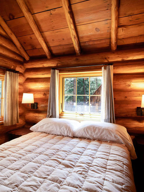 Bed with white bedspread and pillows inside a log cabin with windows