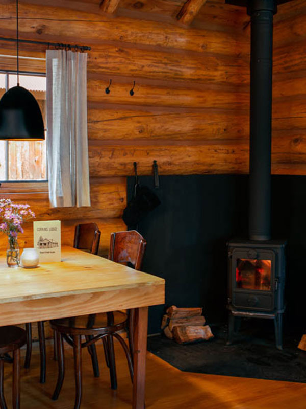 Wood table and chairs and a black wood burning stove in the corner of a log cabin