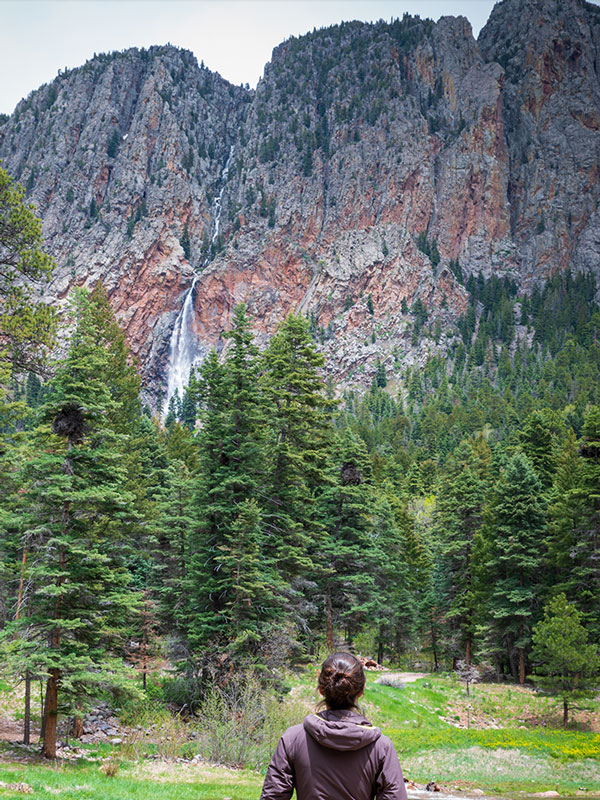 Woman in the foreground looking passt trees at the Brazos Falls waterfall and the cliffs