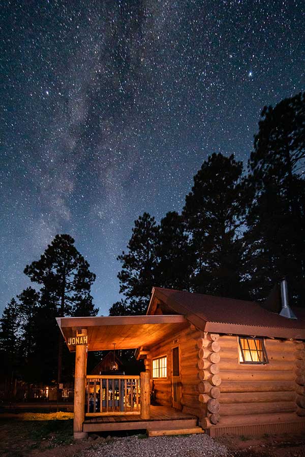 Jonah Log Cabin at night with the milky way stars in the sky above pine trees