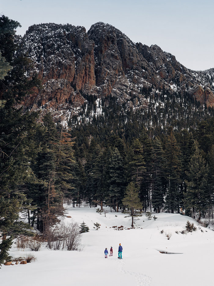 Snowy landscape with three people walking and brazos cliffs in the background