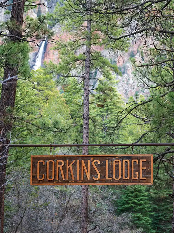 Large wooden sign that says Corkins Lodge hanging with trees in the background