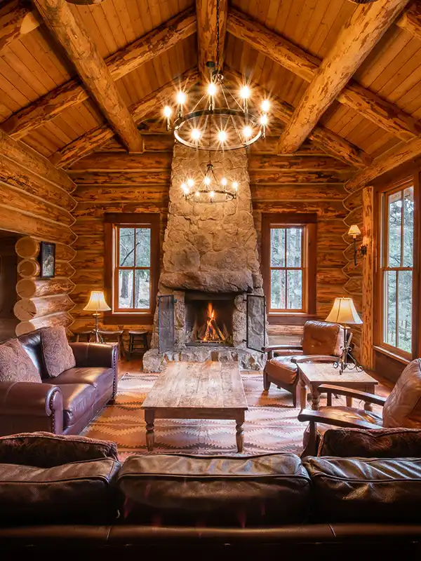Large living room with vaulted ceilings and full-height stone fireplace. Couches, tables, lamps and windows.