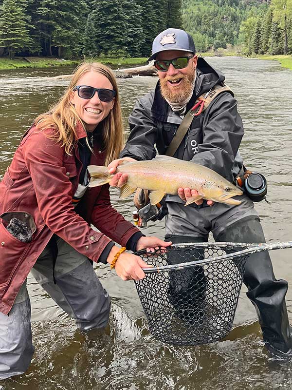 Woman and Man in waders in the river holding a large rainbow trout
