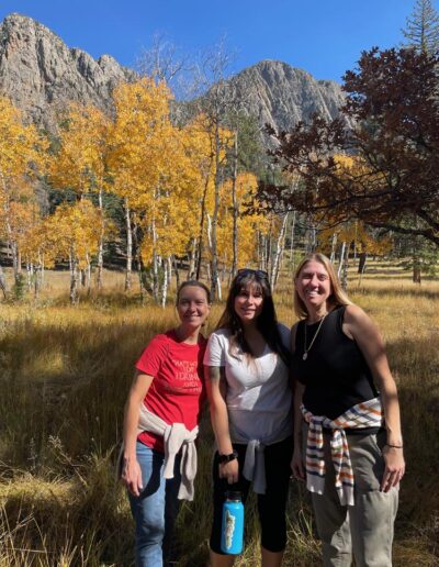 Three women smiling with yellow aspen trees and tall mountains in the background