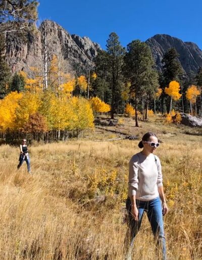 Two women hiking with golden aspen and pine treesand cliffs in the background